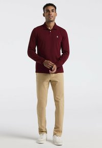 Bordeaux lange mouwen polo met kraag en klein logo, gecombineerd met beige chino's en witte sneakers. Gladde stof en slim fit ontwerp.
