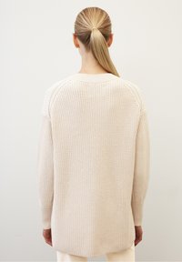 Maglione lavorato a maglia beige con vestibilità ampia, maniche raglan e polsini a costine. Motivo testurizzato con un orlo posteriore più lungo.