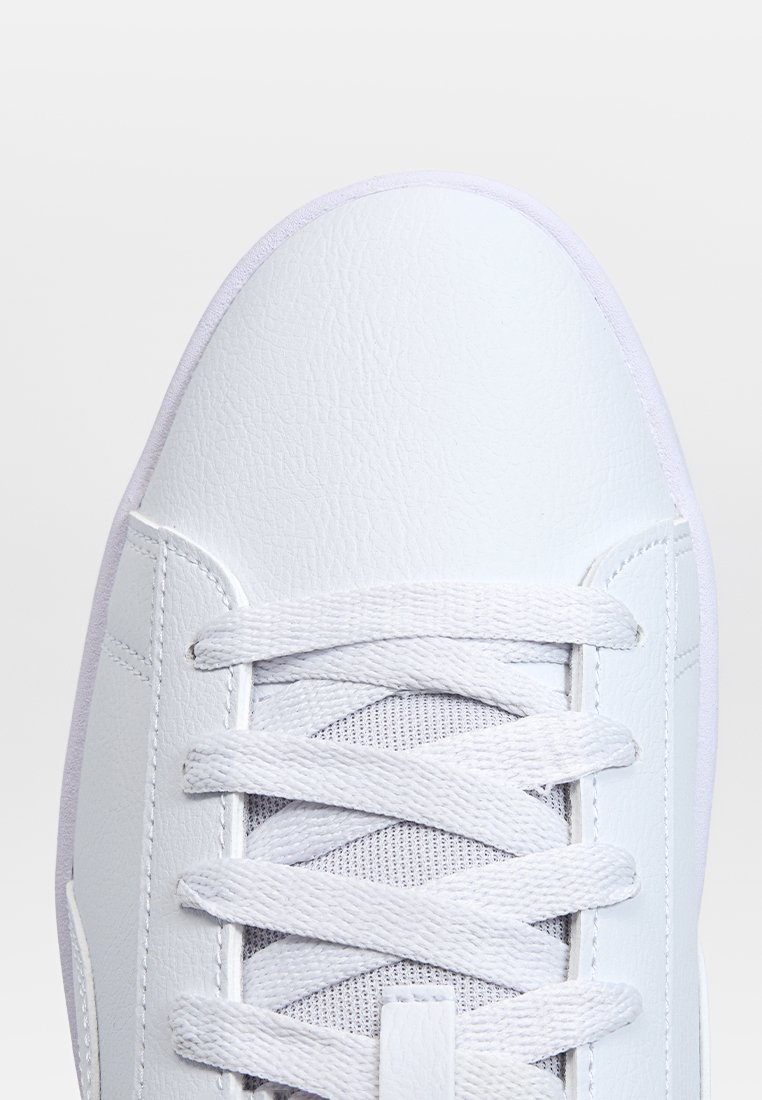 Zapatilla de cuero blanca con una textura suave, cordones planos y lengüeta acolchada. Diseño de punta redonda con detalles de costura sutil.