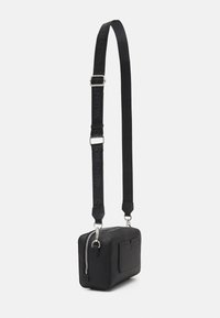 Černá crossbody taška obdélníkového tvaru, vyrobená z texturovaného materiálu. Disponuje zipovým uzávěrem, vnější kapsou a nastavitelným popruhem s logem.