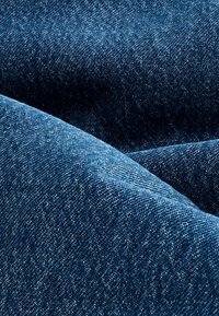Modrá denimu látka s hladkou texturou, s keprovým vzorem a mírným vyblednutím. Povrch vykazuje diagonální vzor, typický pro denim.