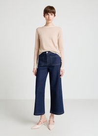 Long-sleeve beige knit shirt with white trim, paired with dark blue wide-leg jeans featuring back pockets and light stitching, complemented by pink heels.
