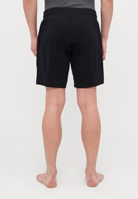 Shorts negri din bumbac, cu o croială relaxată, având un tiv elastic și tăietură curată, văzuți din spate pe un model cu picioarele goale.