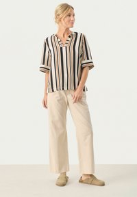 Stribet blouse i beige, sort og orange med V-hals og korte ærmer, parret med lys beige brede bukser og olivengrønne slip-ons.