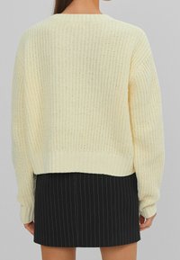 Sweter dziany w bladego żółtego koloru z prążkowaną fakturą i okrągłym dekoltem. Posiada krótki krój i opuszczone szwy ramion.