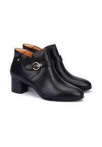 Botas de tobillo de cuero negro con una textura suave, punta afilada y tacón cuadrado. Presentan un acento decorativo de correa circular.