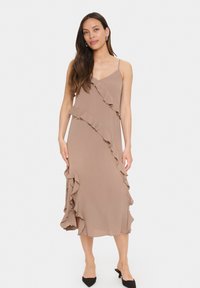 Rochie midi dintr-un material bej deschis, cu accente volănoase de-a lungul unei cusături diagonale. Bretea subțire, croi lejer, cu fante laterale. Purtați cu tocuri negre.