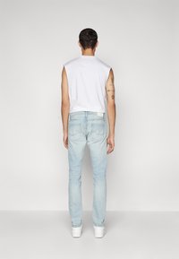 Jeans de mezclilla azul claro con corte slim y top sin mangas blanco, que destaca por su diseño minimalista y detalles en los bolsillos traseros.