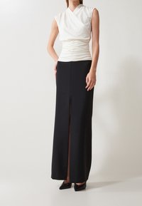 Top blanco con detalle fruncido en la cintura, combinado con una falda larga negra con una abertura frontal. Los tacones son de punta, completando el look.