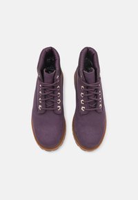 Fioletowe zamszowe botki za kostkę z okrągłym noskiem, beżowymi metalowymi oczkami i pasującymi sznurowadłami. Gumowa brązowa podeszwa i wyściełany kołnierz dla wygody.