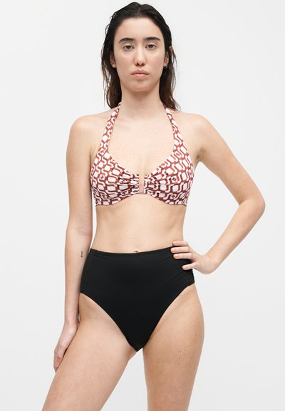 Γυναίκα με μακριά σκούρα μαλλιά, φοράει εμπριμέ τοπ μπικίνι με halter και μαύρο μαγιό με ψηλή μέση, στέκεται με το ένα χέρι στη μέση.