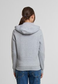 Felpa grigia con cappuccio, realizzata in tessuto morbido, caratterizzata da polsini e orlo a coste, design di lunghezza media e senza loghi o motivi visibili.
