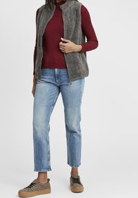 Chaleco de forro polar en gris, camiseta de canalé en burdeos, jeans de color azul claro y zapatillas marrones texturizadas. El chaleco tiene cremallera y bolsillos laterales.