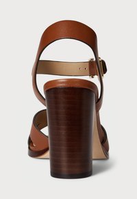 Hnedé kožené sandále na podpätku s hrubým dreveným efektom na podpätku, remienkom okolo členku a béžovým vnútorným podšívkou. Obsahujú minimálne kovové detaily.