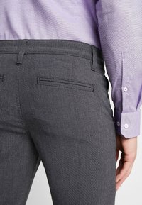 Šedé upravené kalhoty s hladkou texturou, se plochým předním dílem, zadními kapsami a slim fit střihem, spárované se světle levandulovou košilí.
