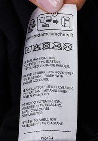 Étiquette d'entretien avec détails sur la composition du tissu : 83 % polyester, 17 % élasthanne. Présence de plusieurs langues. Les étiquettes incluent des instructions de lavage et des symboles.