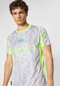 Grå sportsjersey med et vanddråbemønster, lyse neongrønne accenter og logodetaljer. Korte ærmer og rund halsudskæring.