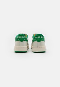 Klasični Reebok športni copati v bež in zeleni barvi, z teksturiranim usnjenim zgornjim delom, oblazinjenim ovratnikom in gumijastim podplatom z zelenimi detajli.