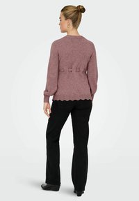 Mākslīgā purpursarkana adīta džemperis ar viļņotu apakšmalu, teksturētu audumu un trim saišu detaļām aizmugurē, apvienots ar melniem platajiem biksēm.