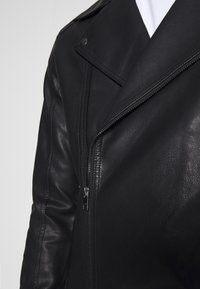 Giacca da motociclista in pelle nera con collo a lancia, chiusura con cerniera asimmetrica, finitura testurizzata e dettagli in metallo color argento.