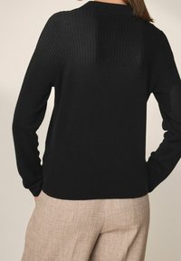 Maglione nero lavorato a maglia con texture a coste, maniche lunghe e colletto, abbinato a pantaloni beige con texture.