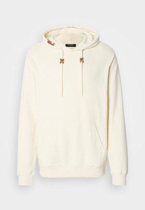 Kreemivärvi ribakoe kä hoodie, eesmine kangaroo tasku, nöörid pruunide aktsentidega ja väike logo silt kapuitsi serval.