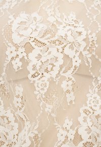 Tissu délicat en dentelle blanche présentant des motifs floraux, des coutures complexes et des détails en maille fine, créant un aspect texturé et superposé.