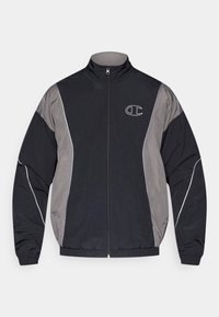 Schwarze und graue Sportjacke mit Reißverschluss, hohem Kragen, elastischen Bündchen, reflektierenden Paspeln und weiß umrandetem "C"-Logo auf der linken Brust.
