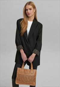 Blazer nero con polsini a righe, abbinato a una borsa tote in pelle intrecciata color beige. Tessuto liscio, vestibilità su misura, chiusura a bottone, design minimalista.