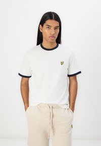 Hvid bomulds t-shirt med marineblå ribbet krave og manchetter, med et lille gult sommerfugl-logo på brystet, parret med beige shorts med snøre.