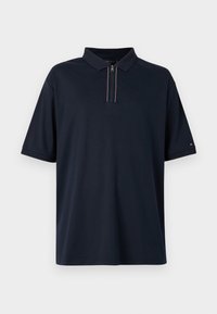 Mørkeblå polo skjorte med frontglidelås og korte ermer. Har klassisk krage og subtile røde og hvite detaljer. Myk stoffoverflate.
