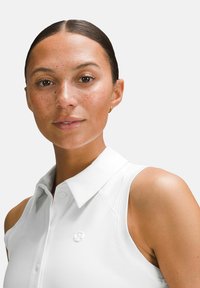 Bijela bezrukava polo majica sa strukturiranim ovratnikom i suptilnom teksturom; sadrži mali logo na prsima.