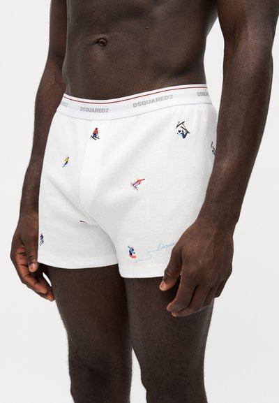 Homme portant un boxer blanc avec de petites figures colorées de ski et de snowboard et une ceinture de marque.