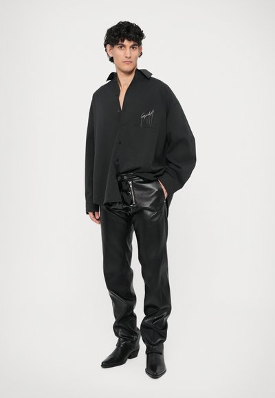 Black oversized button-up shirt with a chest pocket, paired with glossy black leather pants and pointed black boots.