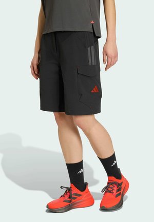 Person wearing black cargo shorts with red logo, black socks with white stripes, and bright red running shoes with black laces.