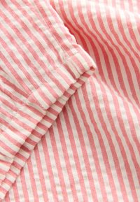 Tessuto a righe rosse e bianche con una texture morbida. Le righe sono sottili e distanziate uniformemente, con una finitura semplice alla cucitura.