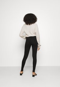 Jeans skinny negros de tiro alto con una textura suave, combinados con un suéter de punto ligero en color beige y sandalias de tacón bajo.