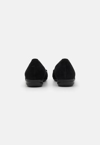 Ballerine in pelle scamosciata nera con punta arrotondata e suola bassa in gomma. Presentano una texture liscia e un design minimalista.
