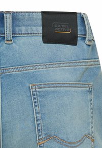 Jasnoniebieskie jeansy z denimu pokazujące tylną kieszeń oraz czarną metkę marki Camel Active przyszytą do pasa.