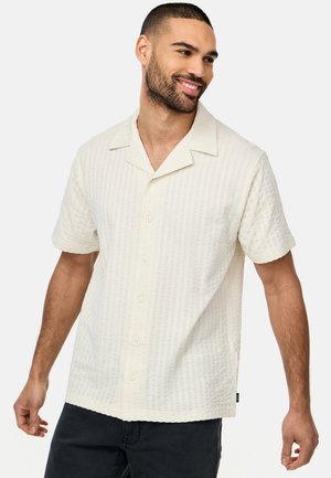 Camisa de manga corta en crema clara con un patrón texturizado de canalé, cuello y botones en la parte delantera, con un corte relajado.