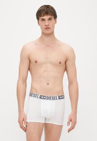 Valged bokserid halli vööga, millel on "DIESEL" logo, valmistatud siledast ja venivast materjalist, mis on mõeldud mugavuseks.
