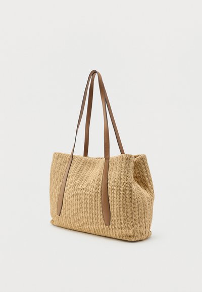 Μπεζ υφασμάτινη τσάντα ώμου με μακριά καφέ δερμάτινα λουριά, ορθογώνιο σχήμα και απαλό, υφή υφάσματος σε λευκό φόντο.