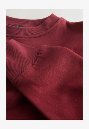 Hanorac burgundy cu guler și manșete ribbed. Textură netedă cu o ușoară strălucire, punând în evidență cusăturile și un material moale, confortabil.