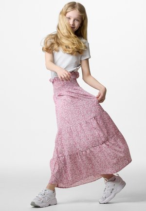 Rosa Blumen-Maxi-Rock mit einem gesmockten Bund, gestuften Lagen und leichtem Stoff. Kombiniert mit weißen Sportschuhen.