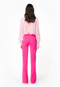 Roze blouse met paisleyprint en lange mouwen met volants, gecombineerd met felroze, nauwsluitende broek, gezien vanaf de achterkant.