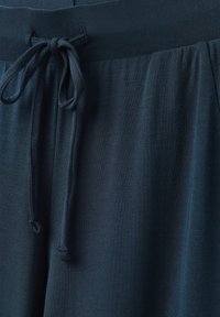 Granatowe spodnie dresowe o miękkiej strukturze, z elastycznym pasem i sznurkiem do regulacji. Tkanina ma gładkie, matowe wykończenie.