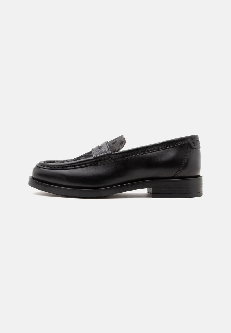 Mocassin en cuir noir avec un petit talon et une bride texturée sur le coup de pied sur fond blanc uni.