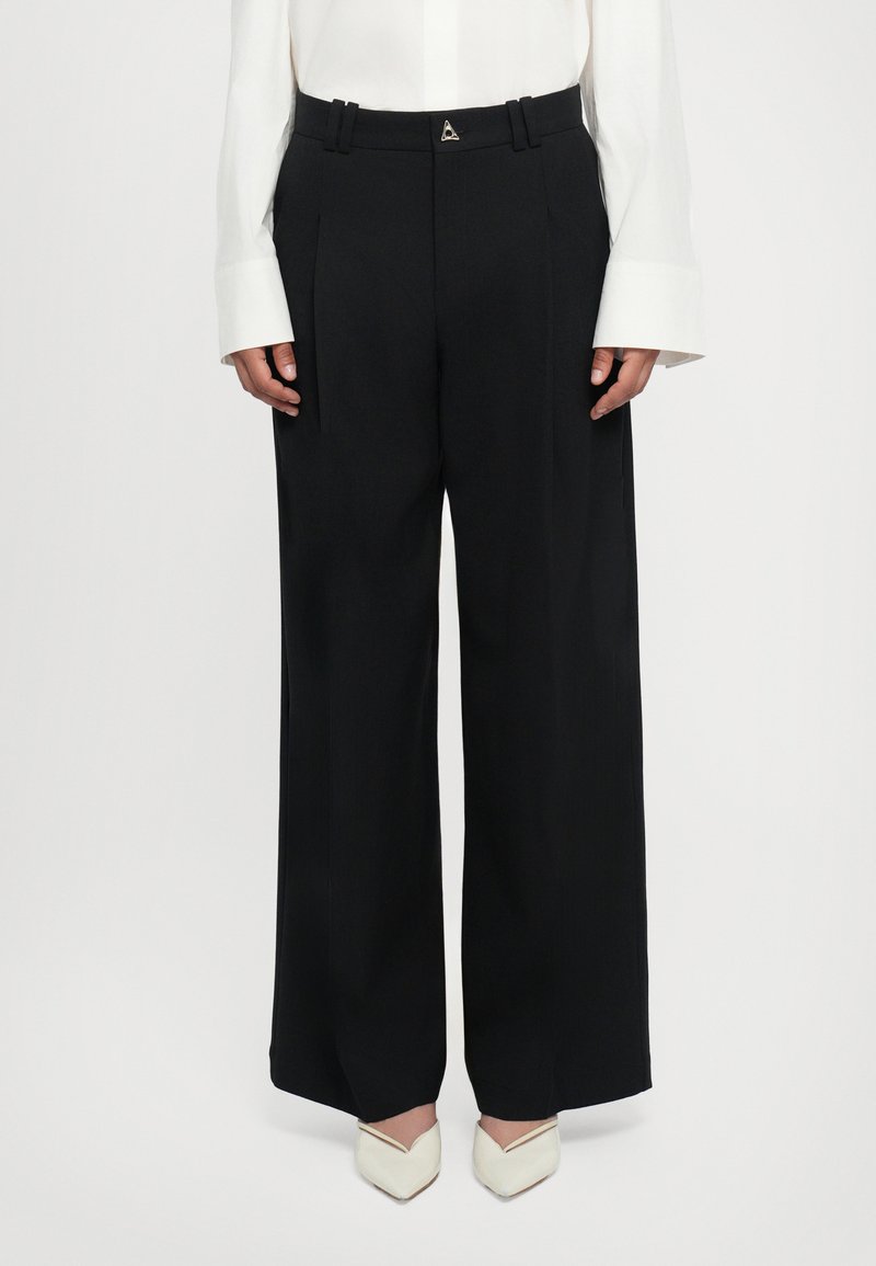 Black wide-leg trousers with pleats, featuring a silver triangle accent at the waist. Smooth fabric texture complements the structured design.