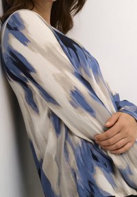 Blouse légère présentant un mélange de couleurs bleu, gris et crème dans un motif marbré. Manches longues et texture douce pour un confort optimal.