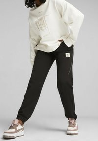 Vit oversized sweatshirt med guldtext, tillsammans med svarta avsmalnande byxor med ficka och dragkedja. Skor: beige och rosa sneakers.